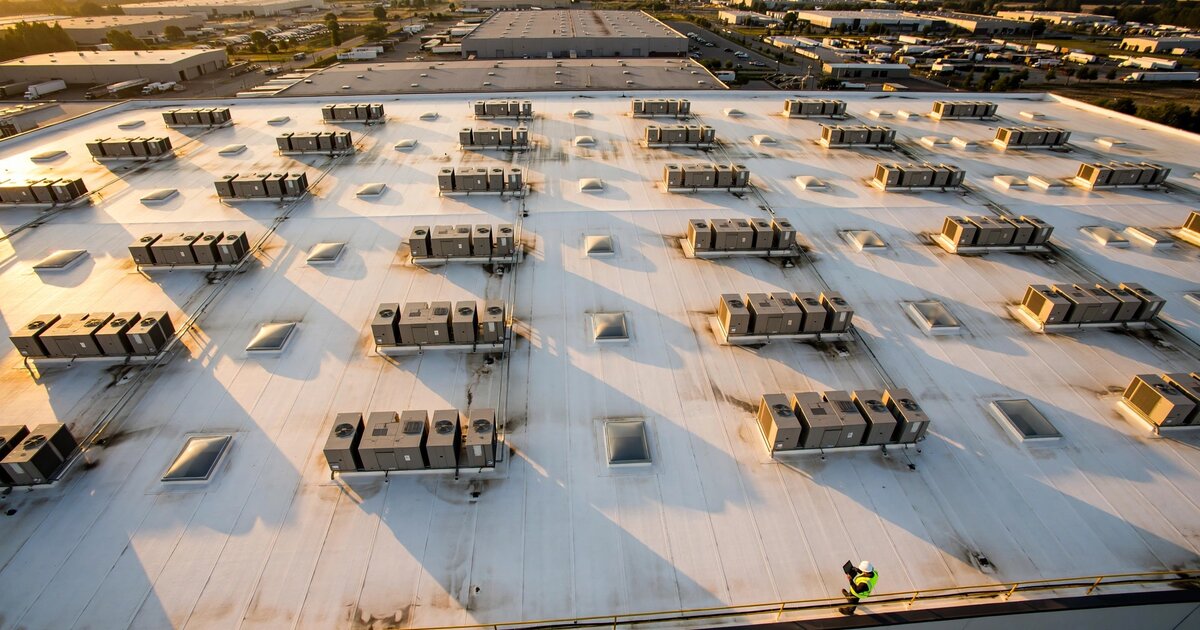 Aerial view of commercial warehouse rooftop with facility manager reviewing tablet