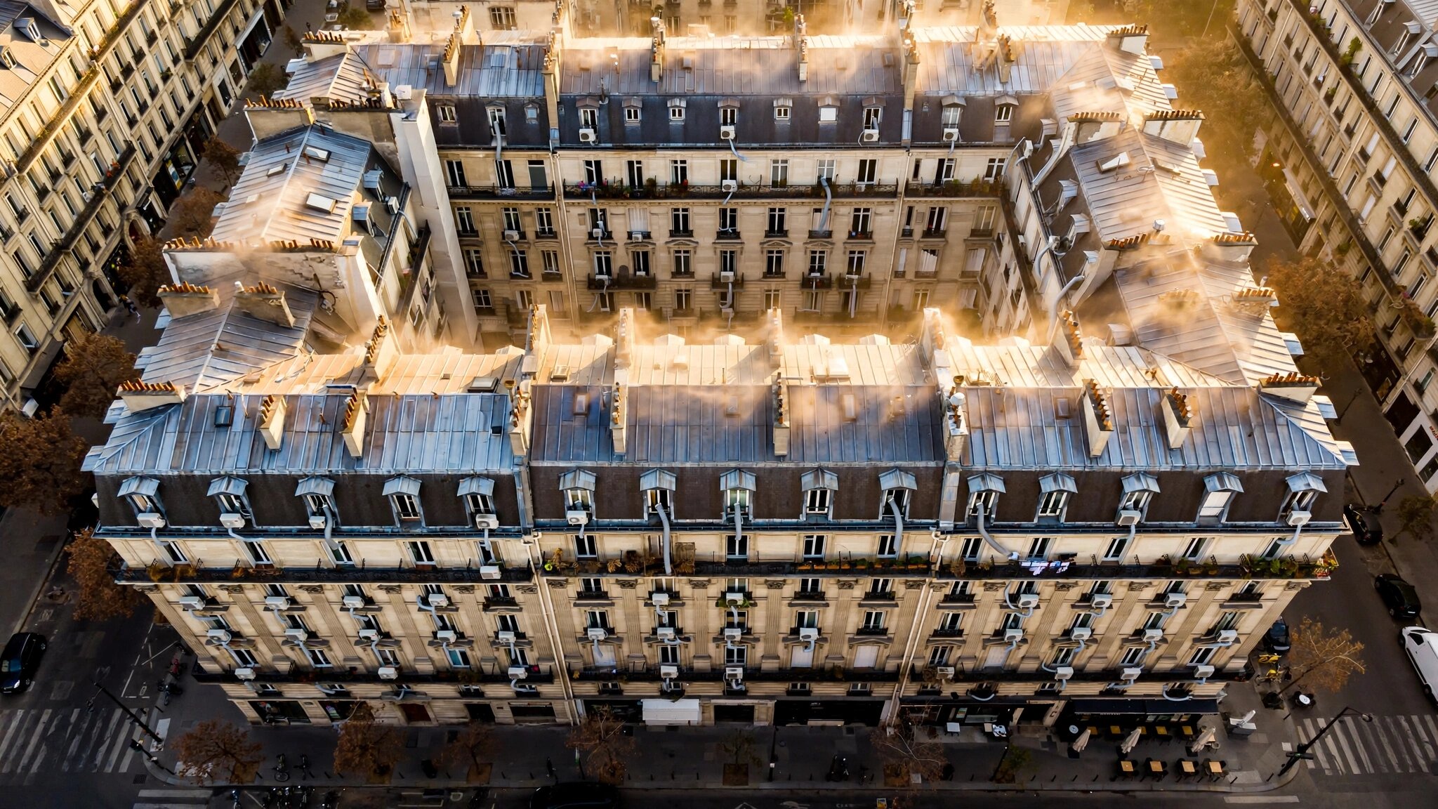 Aerial view of ornate 19th-century European apartment buildings in summer heat, portable AC units visible in windows contrasting with classical stone facades